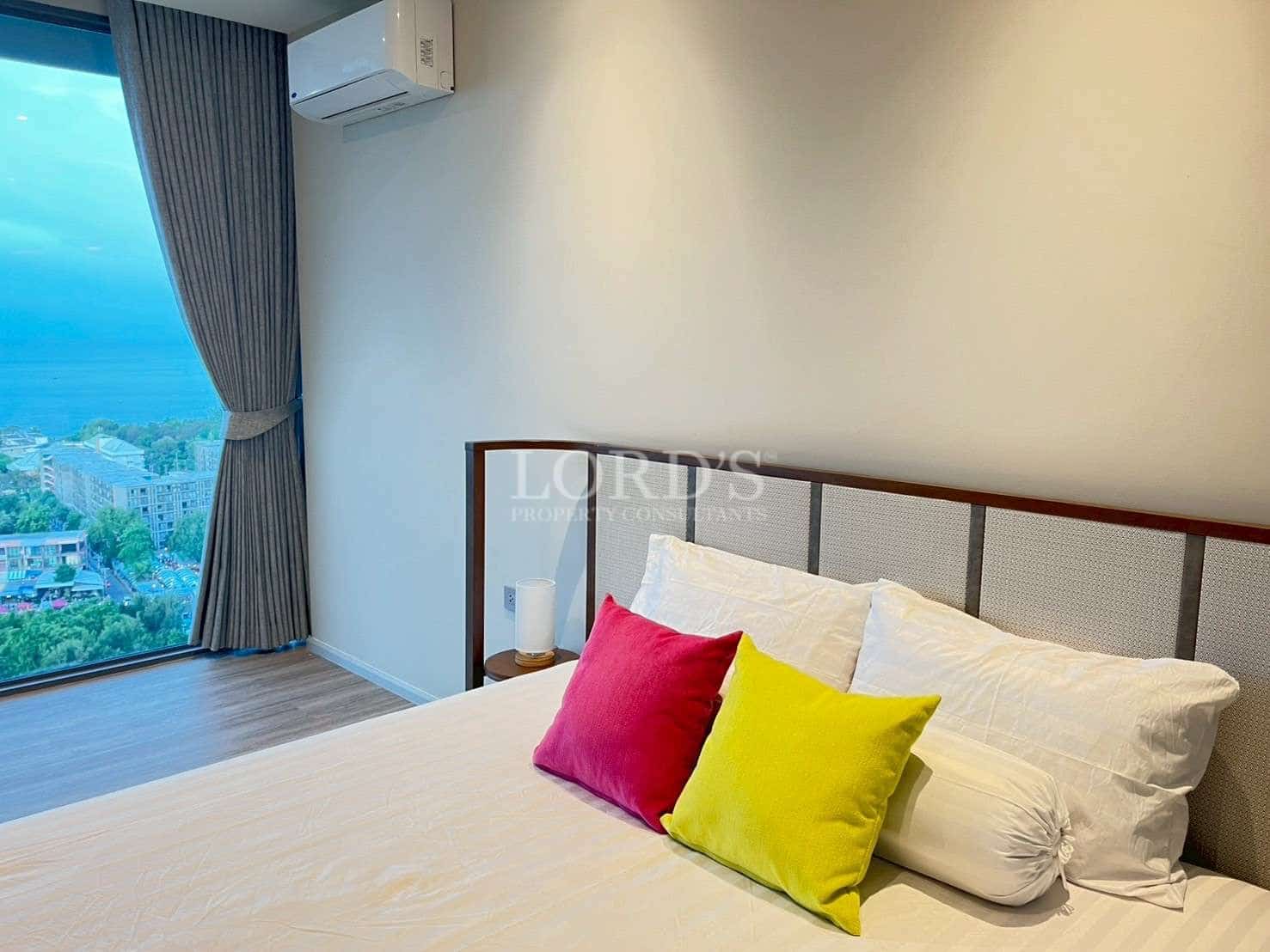 Modern bedroom with comfortable bed, colorful cushions, and large window with city view.