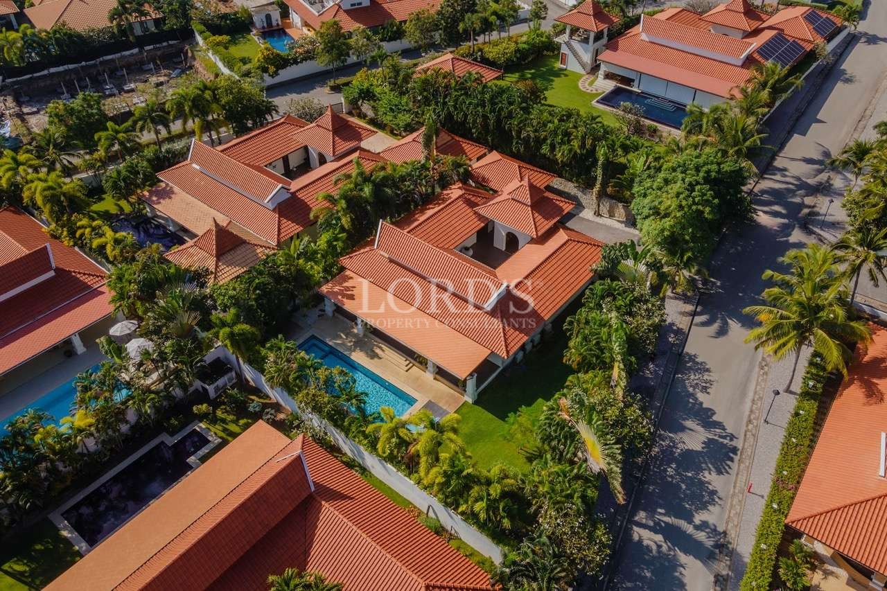 Aerial view of luxury villas with red-tiled roofs, private swimming pools, and palm-lined streets in a tropical residential community.