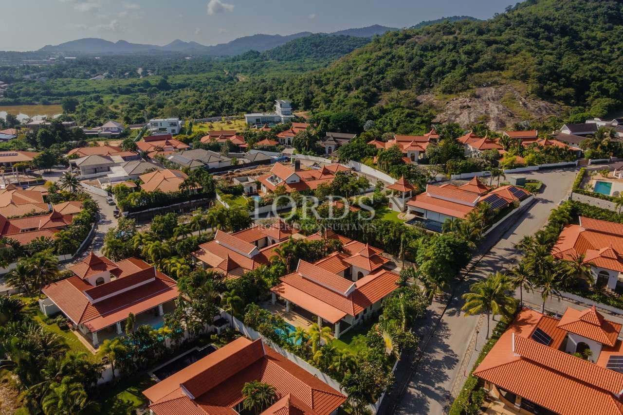 Aerial view of a luxury residential villa community with red-tiled roofs surrounded by hills and tropical greenery.