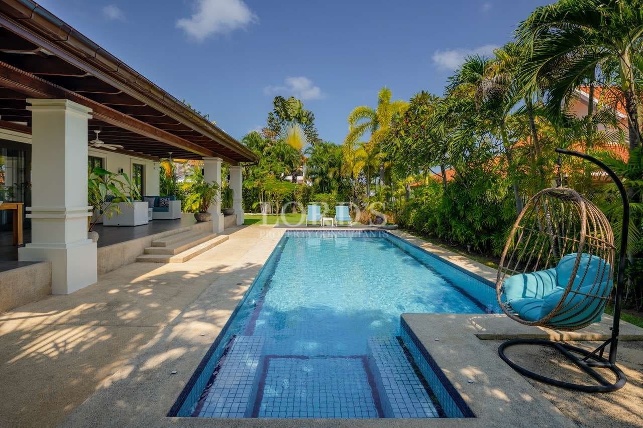 Luxury private villa swimming pool with shaded terrace, tropical garden, and hanging outdoor lounge chair.