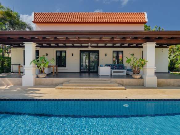 Luxury villa with covered terrace and swimming pool, featuring tropical landscaping and modern outdoor seating.