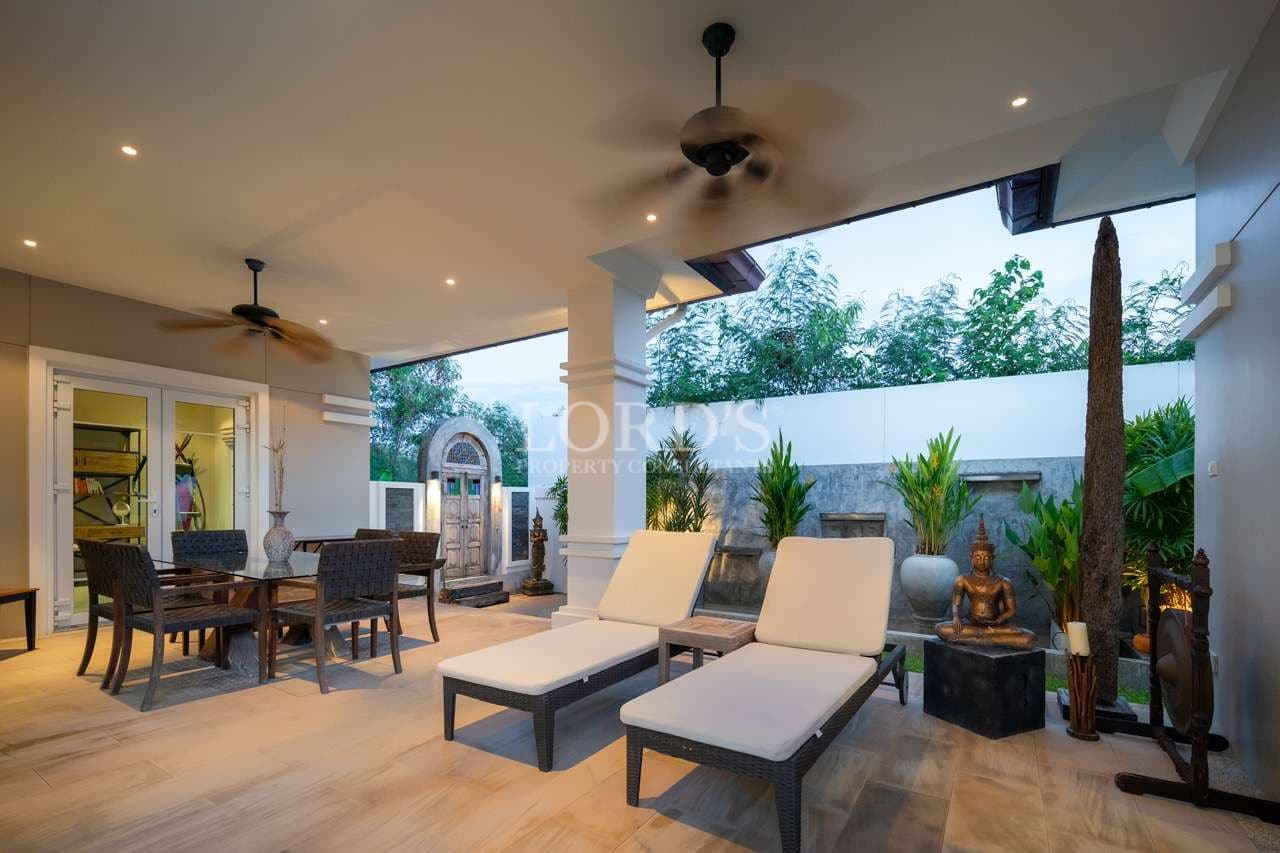 Luxury villa patio with outdoor lounge chairs, dining area, ceiling fans, and tropical garden decor.