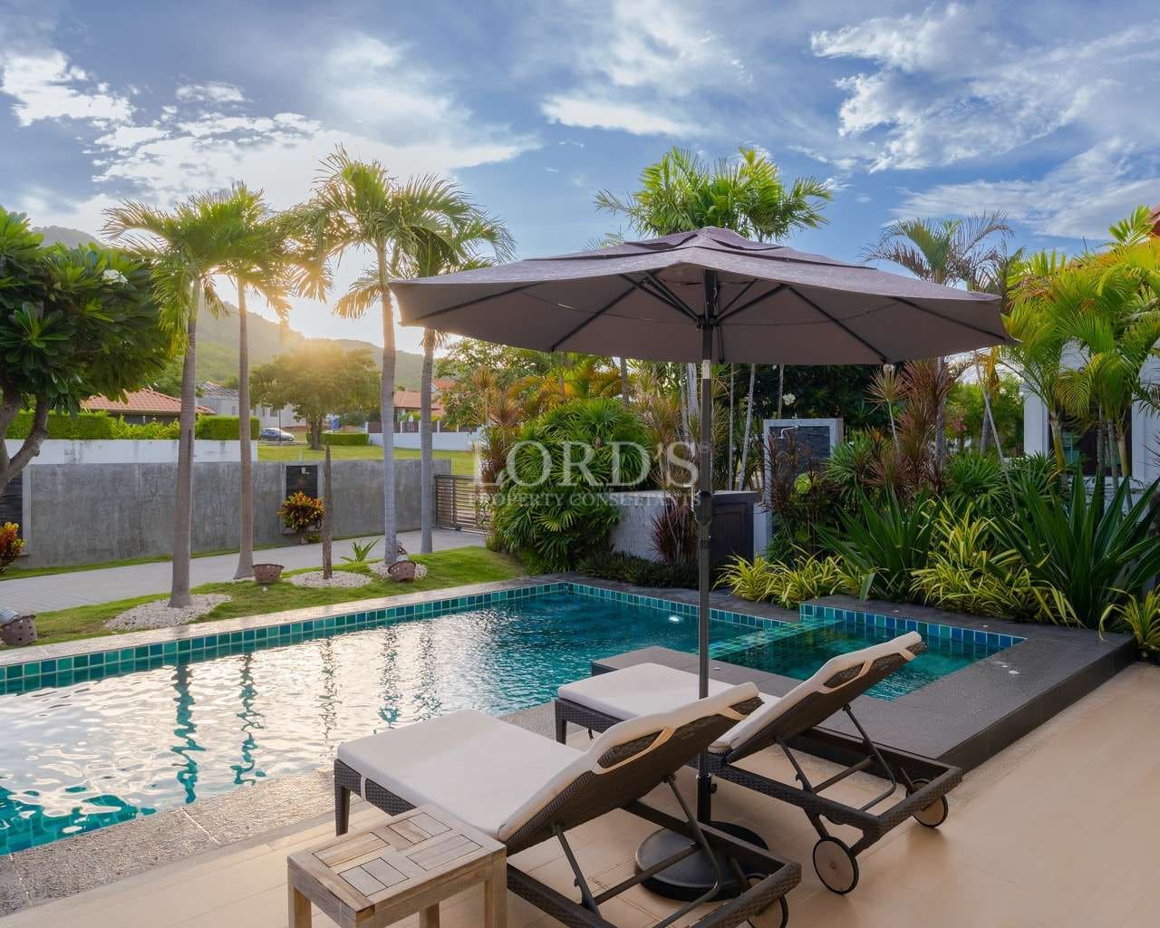 Modern luxury villa with a private swimming pool, sun loungers, and tropical garden under a clear blue sky.