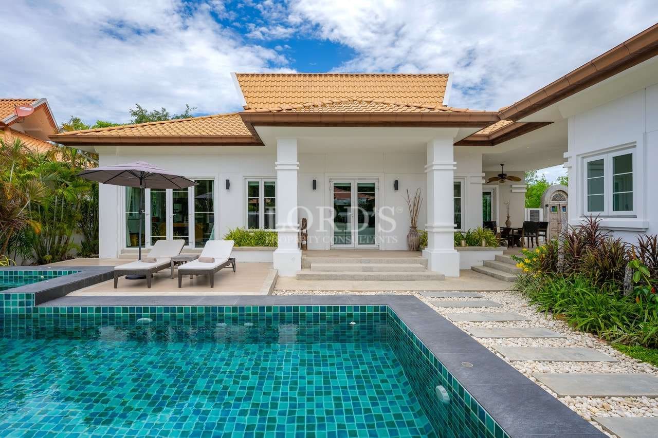 Luxury villa exterior with private swimming pool, sun loungers, tiled roof, and landscaped garden.