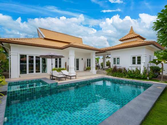 Luxury modern villa with private swimming pool, sun loungers, and landscaped tropical garden under blue sky.