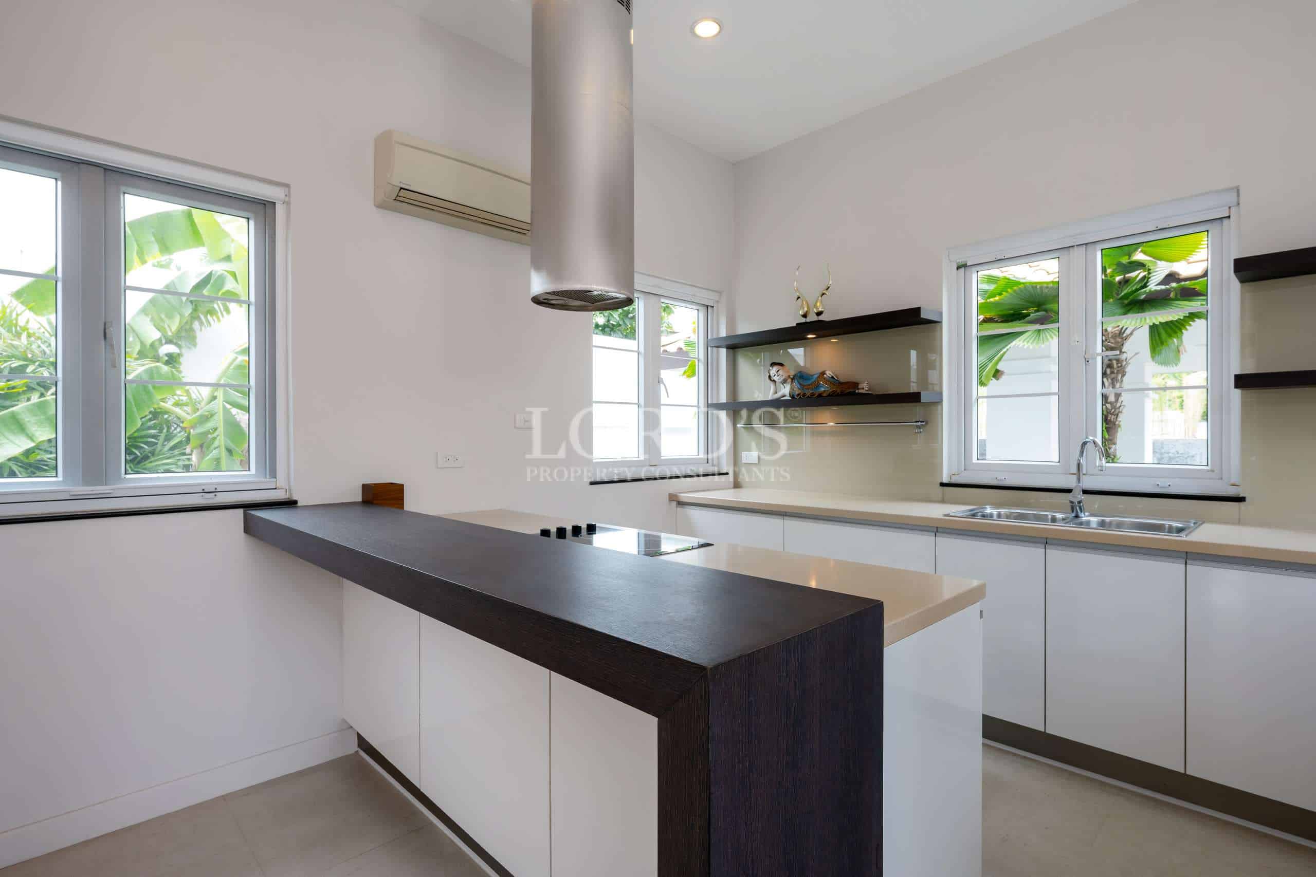 Modern villa kitchen with island counter, white cabinetry, stainless hood, and garden-view windows.