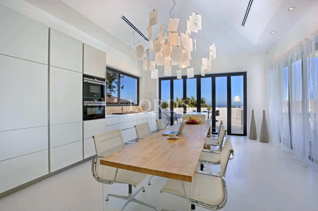 Modern luxury dining room with minimalist kitchen, wooden dining table, designer chandelier, and floor-to-ceiling glass doors.