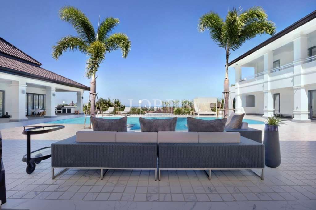 Luxury villa poolside lounge with outdoor sofa seating, palm trees, and modern white villas.