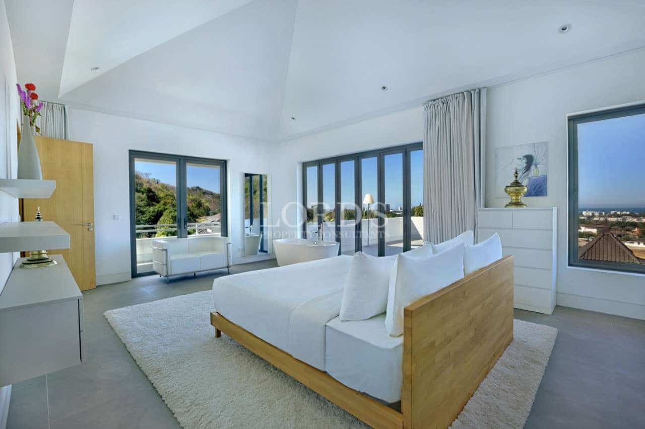 Luxury master bedroom with panoramic windows, minimalist décor, and hillside views.
