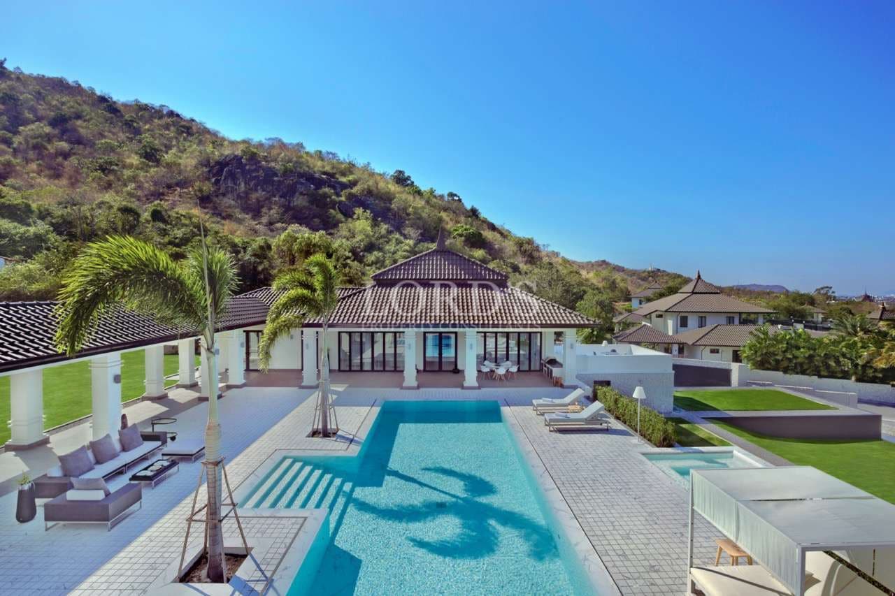 Luxury hillside villa with large swimming pool, palm trees, and panoramic mountain views.