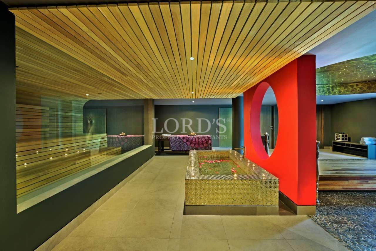 Luxury spa interior with wooden slatted ceiling, mosaic soaking pool, and modern red accent wall.