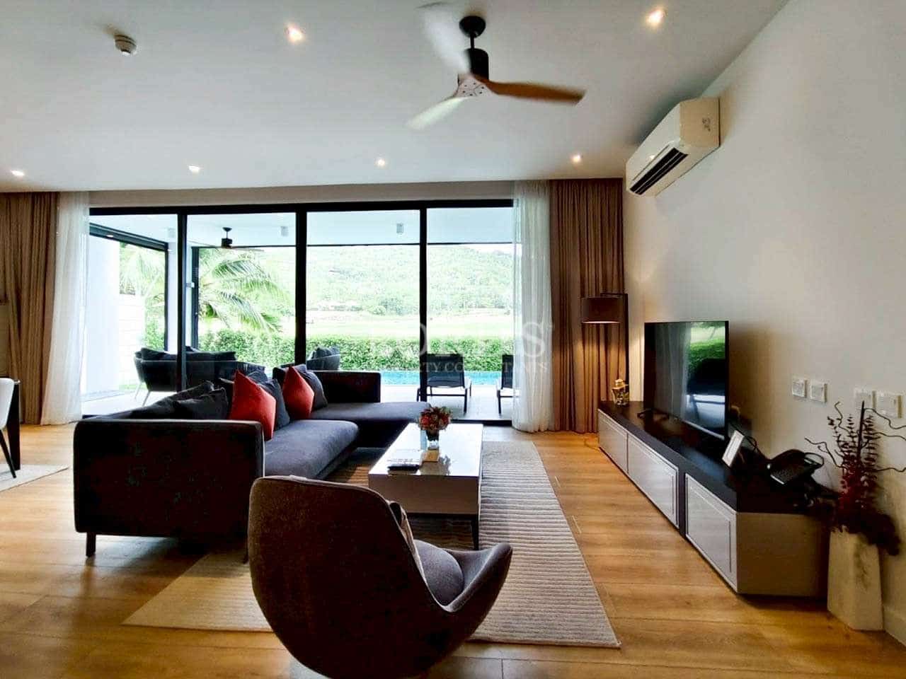 Modern living room with sectional sofa, ceiling fan, wooden flooring, and large glass doors opening to garden