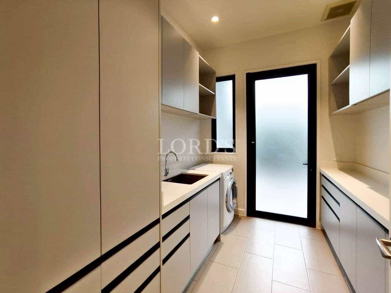 Modern laundry room with built-in cabinets, washing machine, sink, and frosted glass door