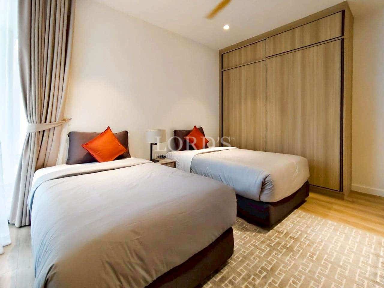 Twin bedroom with two single beds, wooden wardrobe, soft lighting, and neutral décor