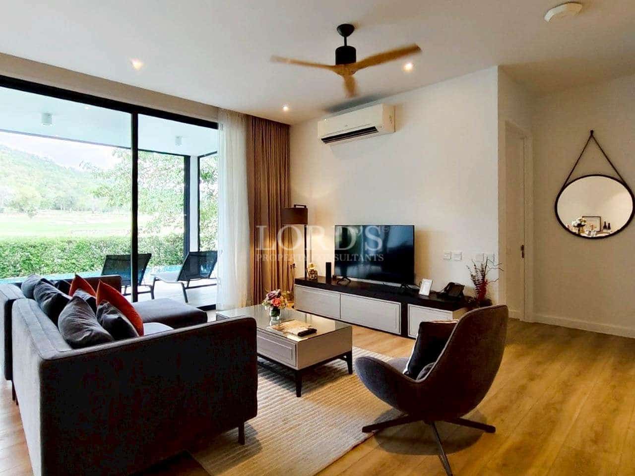 Modern living room with sofa seating, TV console, ceiling fan, wooden flooring, and garden view