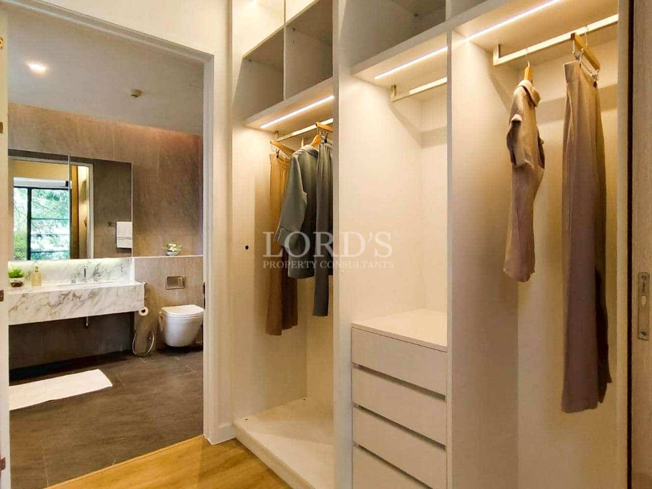 Walk-in wardrobe with built-in storage, hanging space, soft lighting, and adjacent modern bathroom