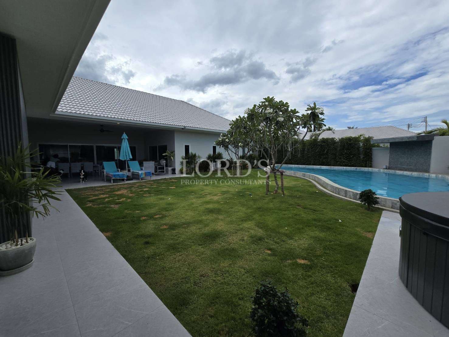 Private villa garden with swimming pool, lawn, and covered outdoor seating area.