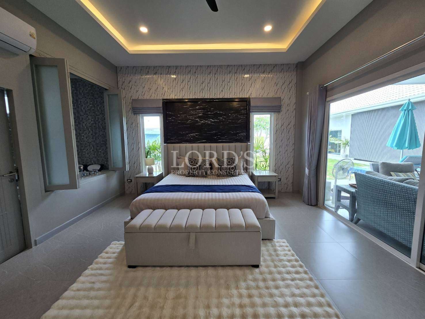 Luxury master bedroom with upholstered bed, accent wall, LED ceiling lighting, and sliding glass doors to outdoor seating.