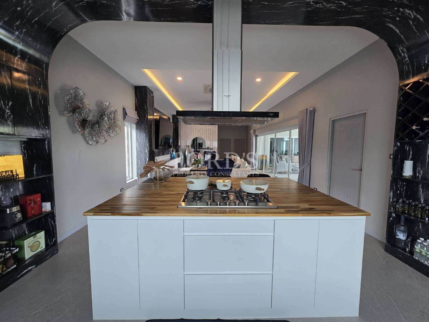 Luxury kitchen with central island, built-in cooktop, wooden countertop, modern cabinetry, and architectural arch design.