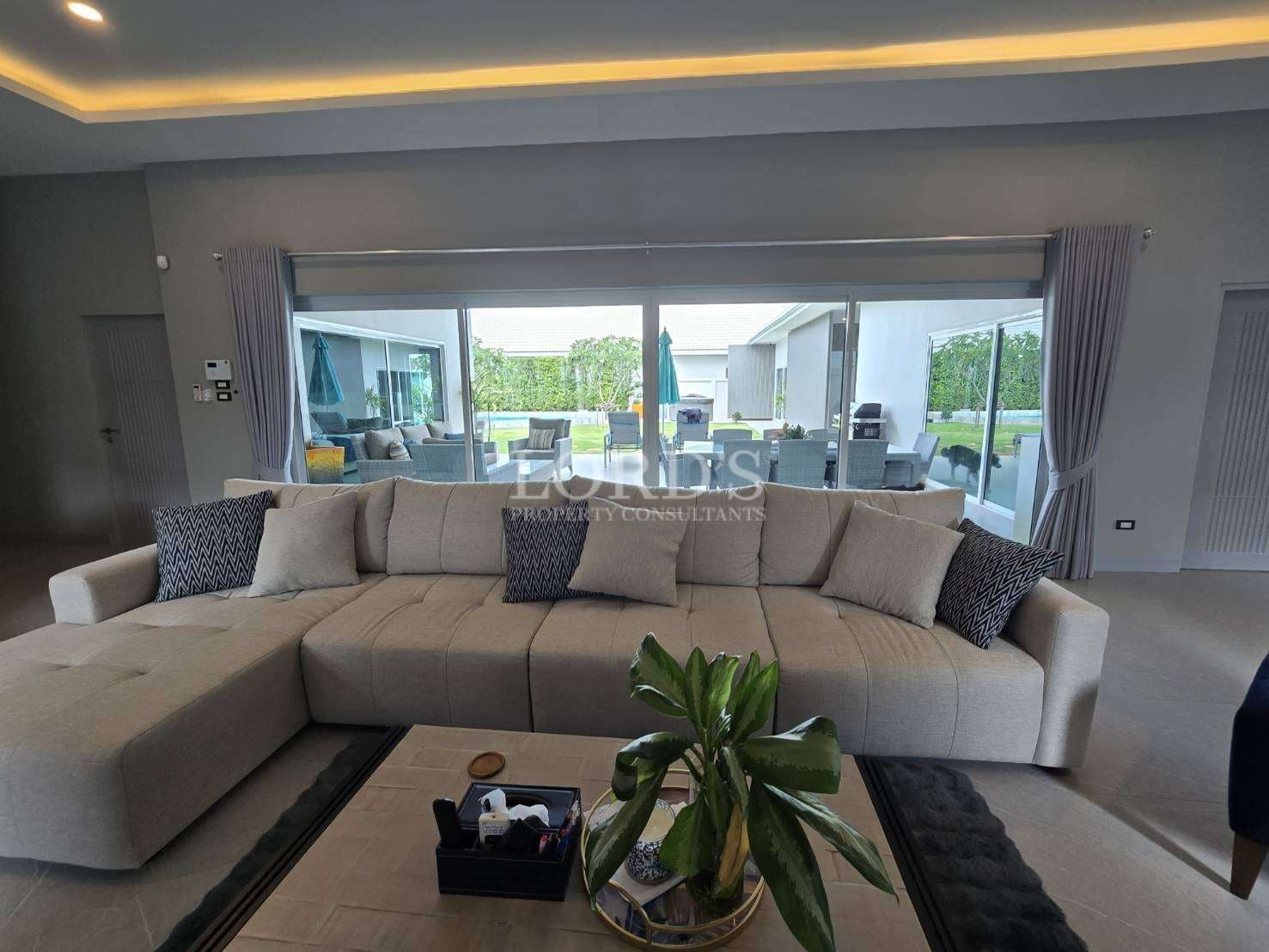 Luxury living room with large sectional sofa, LED ceiling lighting, and sliding glass doors opening to outdoor seating.