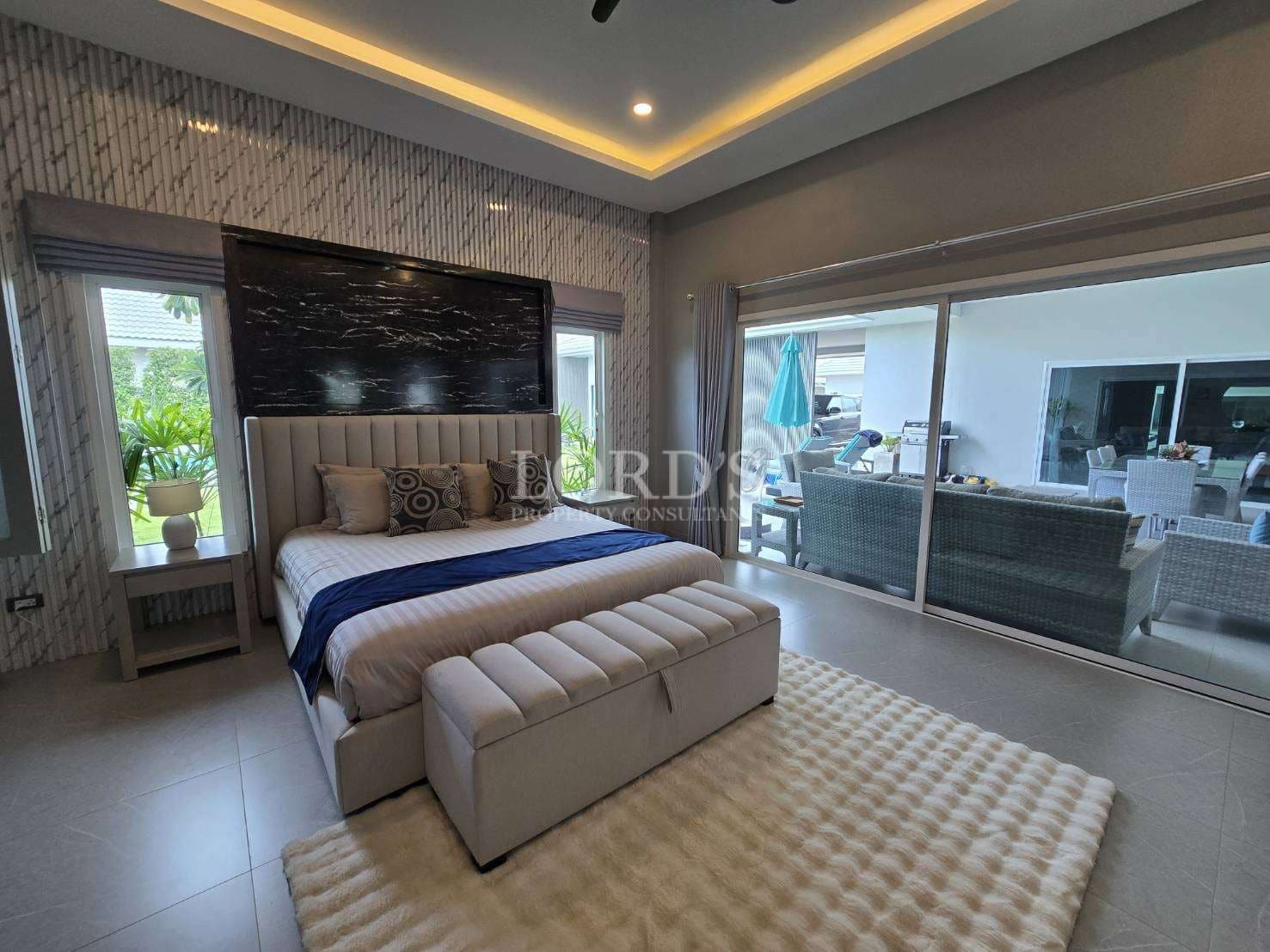 Luxury master bedroom with upholstered bed, accent wall, LED ceiling lighting, and sliding glass doors to outdoor seating.