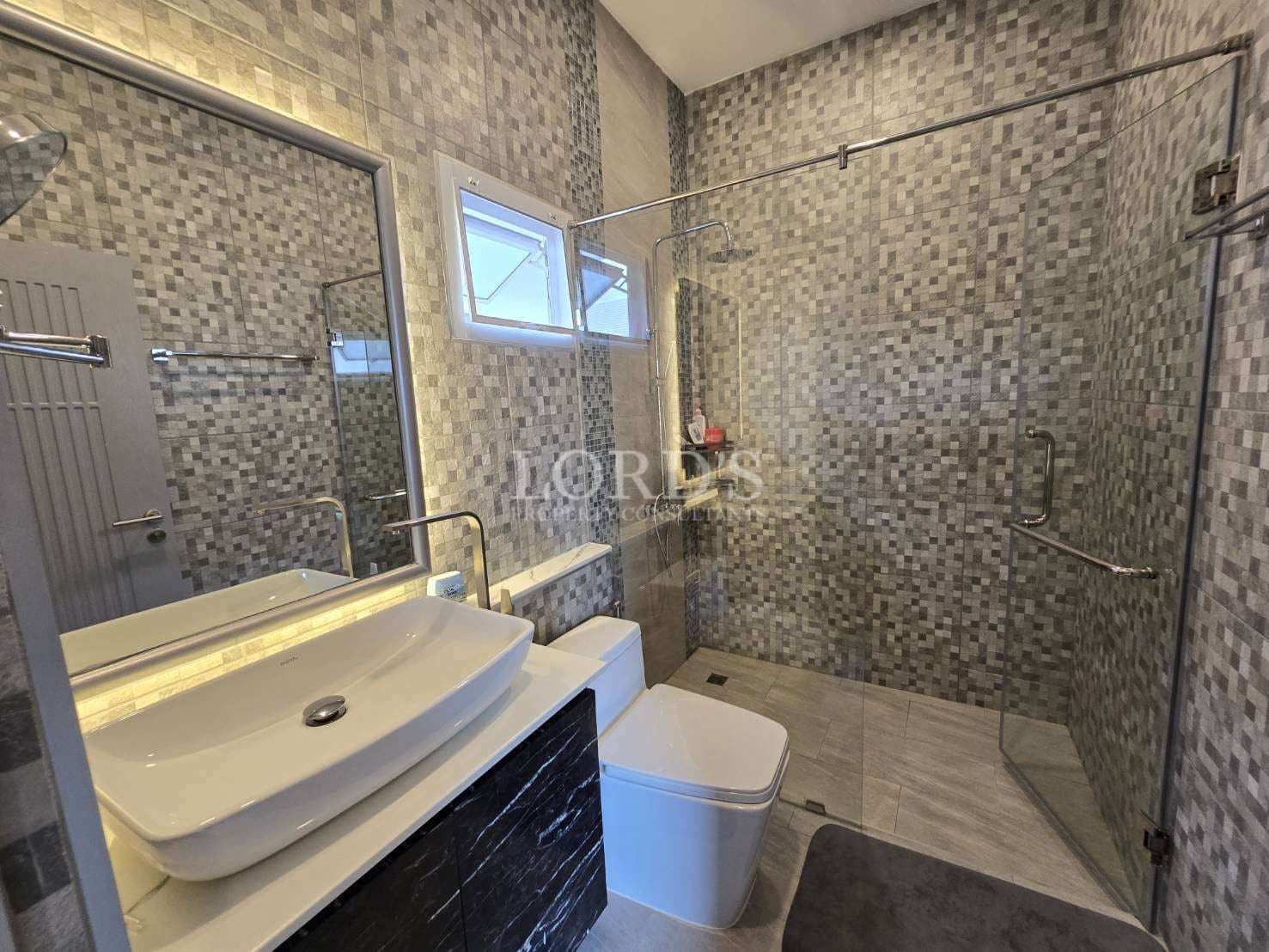 Modern bathroom with walk-in glass shower, mosaic tile walls, vanity sink, and contemporary fixtures.