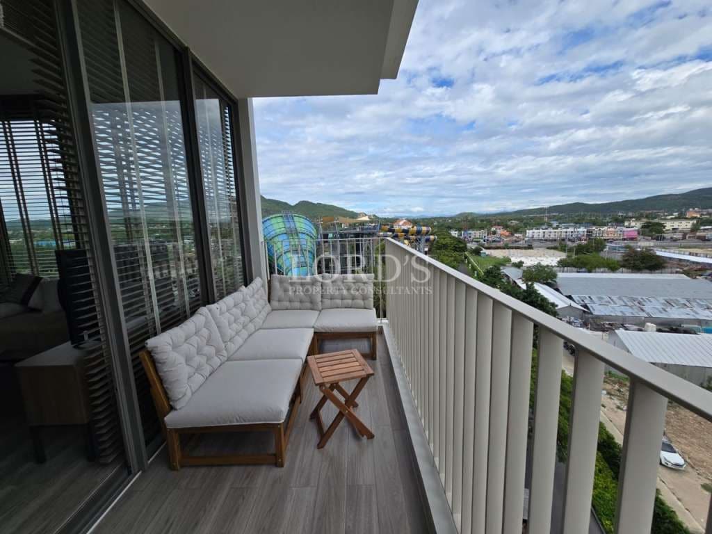 Privater Balkon mit Sitzgelegenheiten im Freien, Blick auf die Stadt und die Hügel, Glasschiebetüren und modernes Wohnungsdesign.