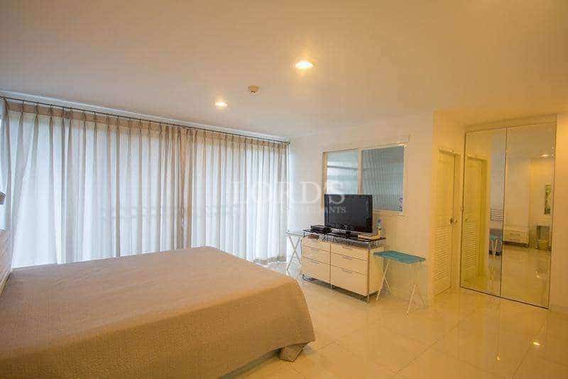 Bright modern bedroom with large bed, floor-to-ceiling curtains, TV unit, and mirrored wardrobe