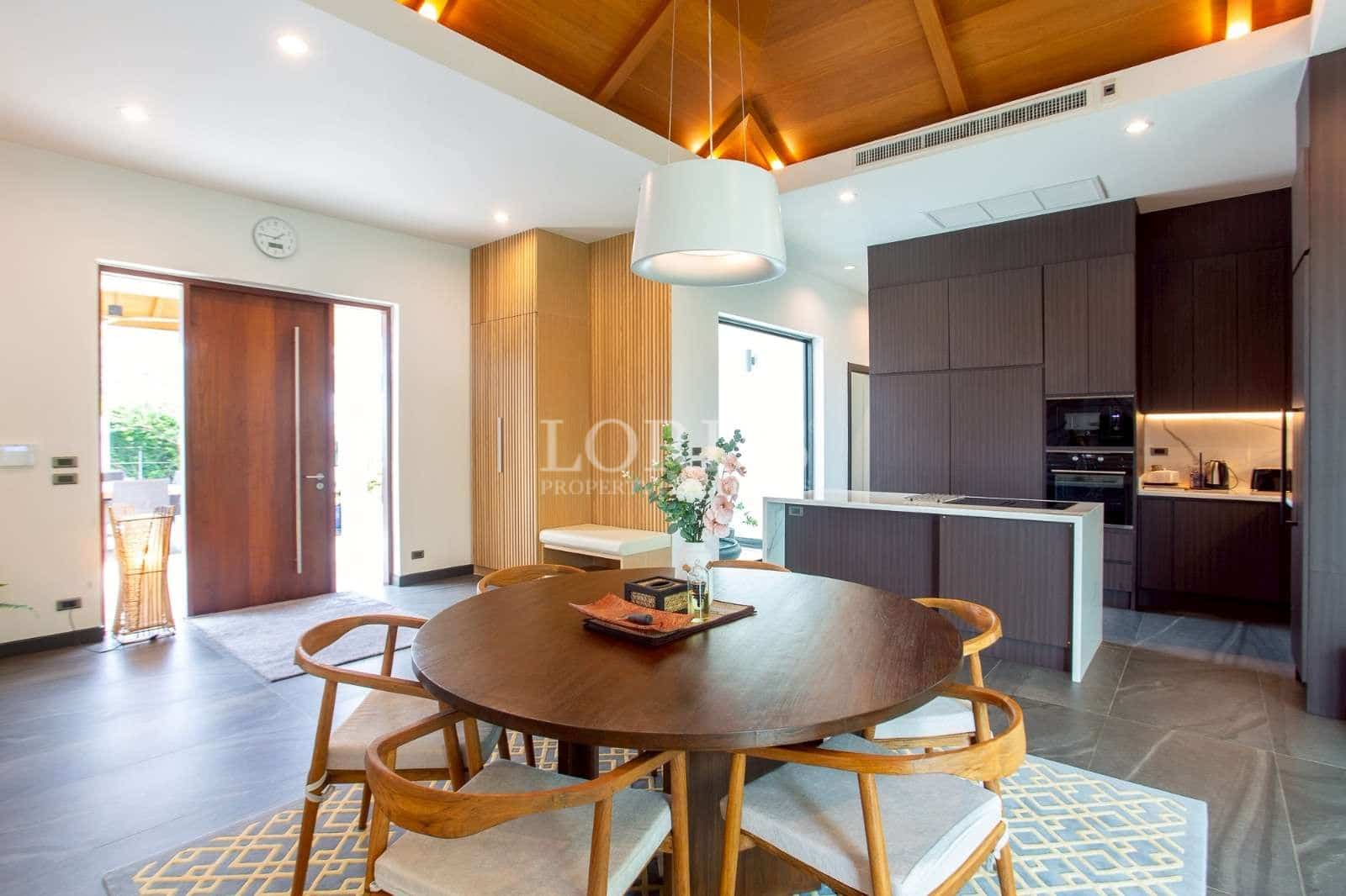 Modern open-plan dining area with wooden ceiling, pendant lighting, and contemporary kitchen.