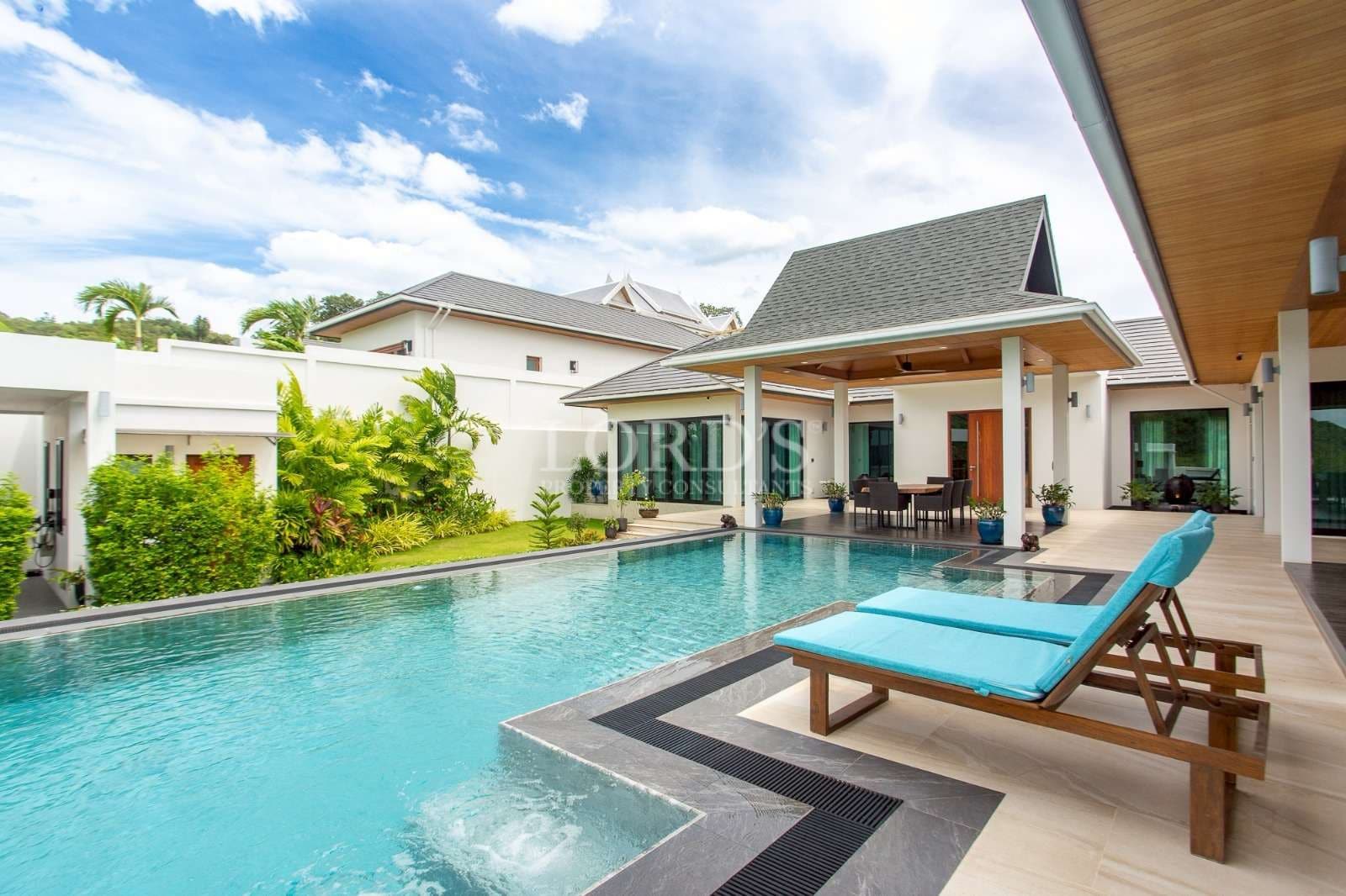 Modern luxury villa with private swimming pool, sun loungers, and covered outdoor dining area.