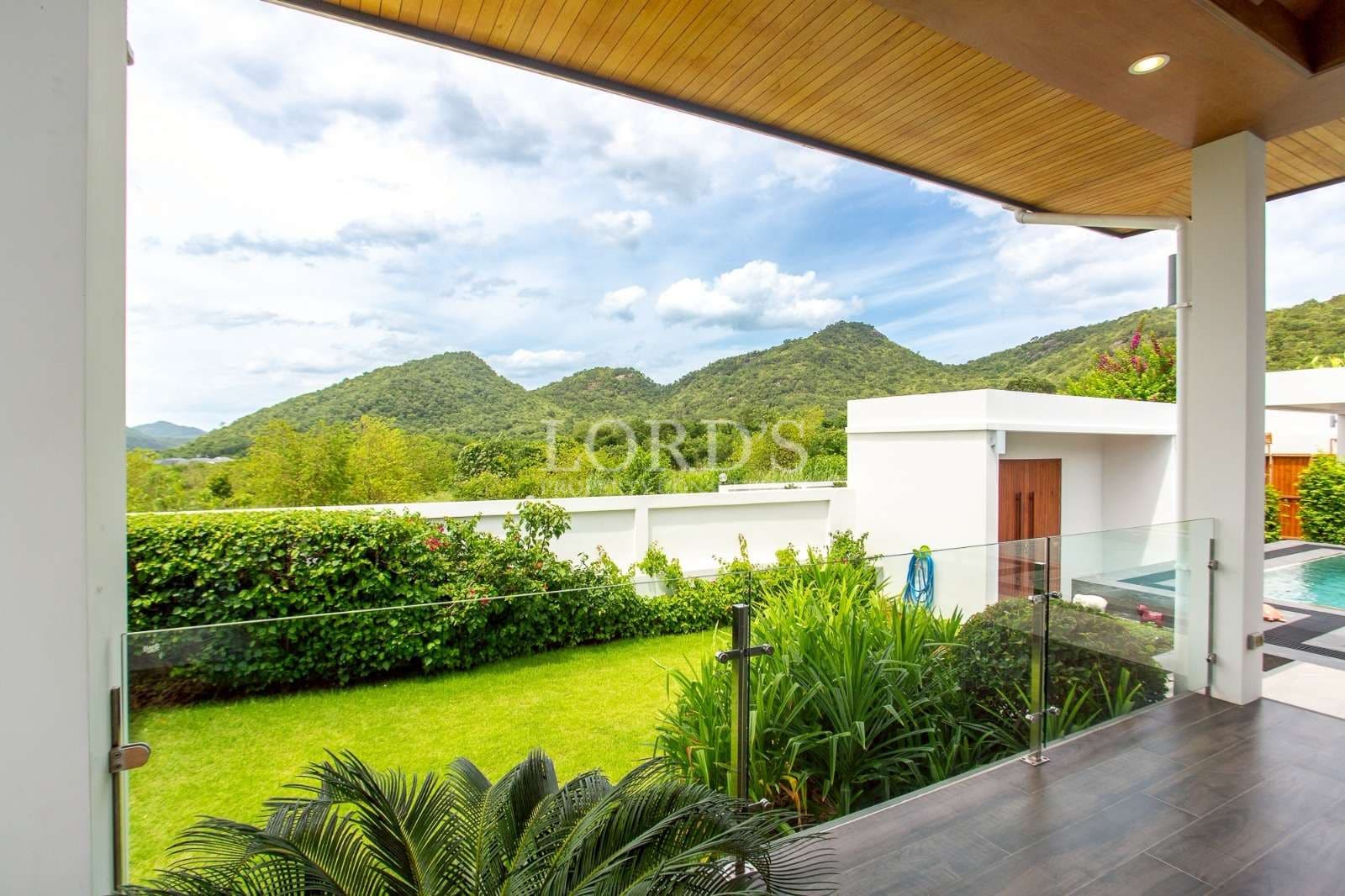 Modern villa terrace overlooking landscaped garden and green mountain views with glass railing.