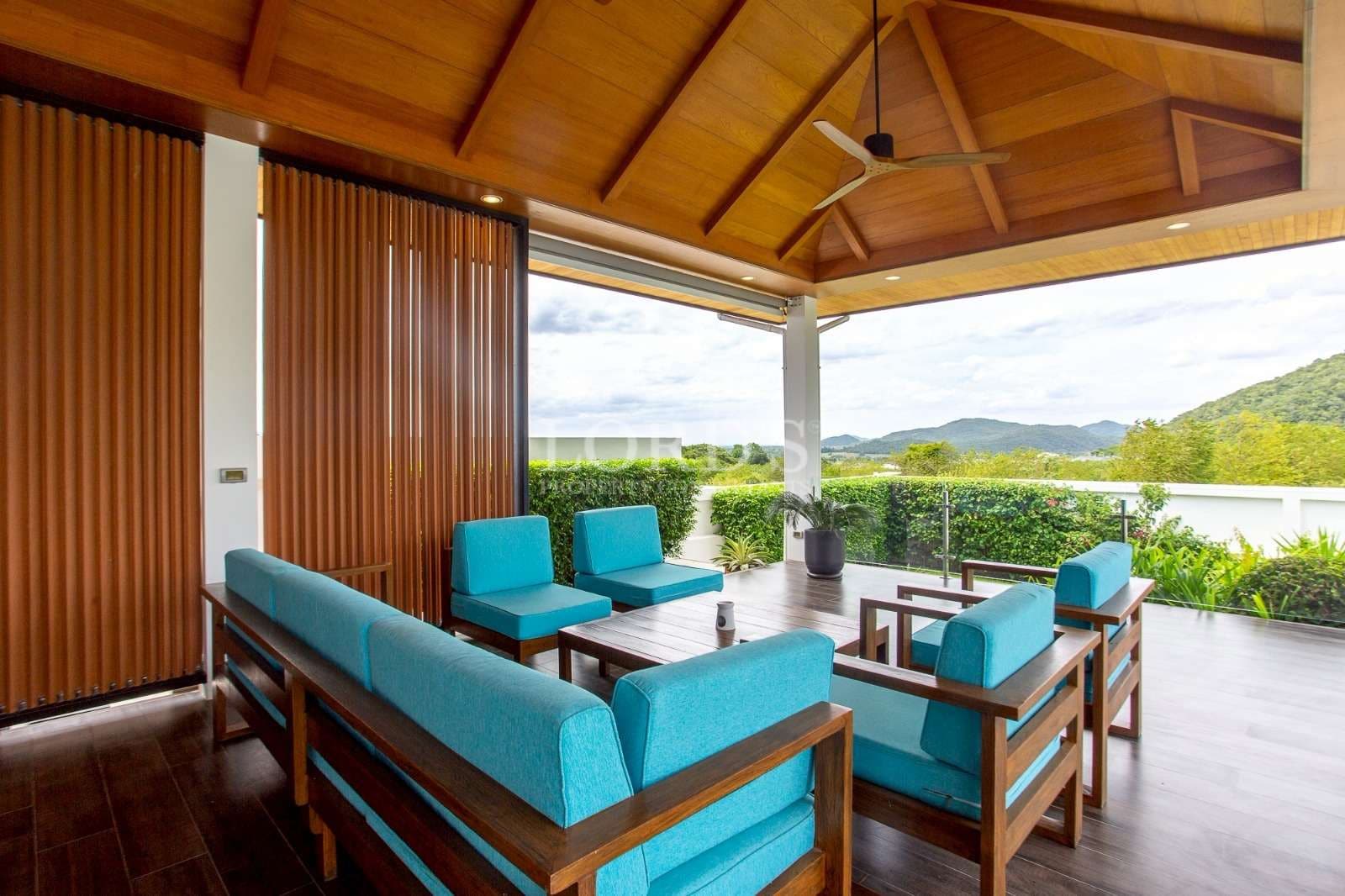 Covered outdoor patio with wooden ceiling, teal seating, and scenic garden views.