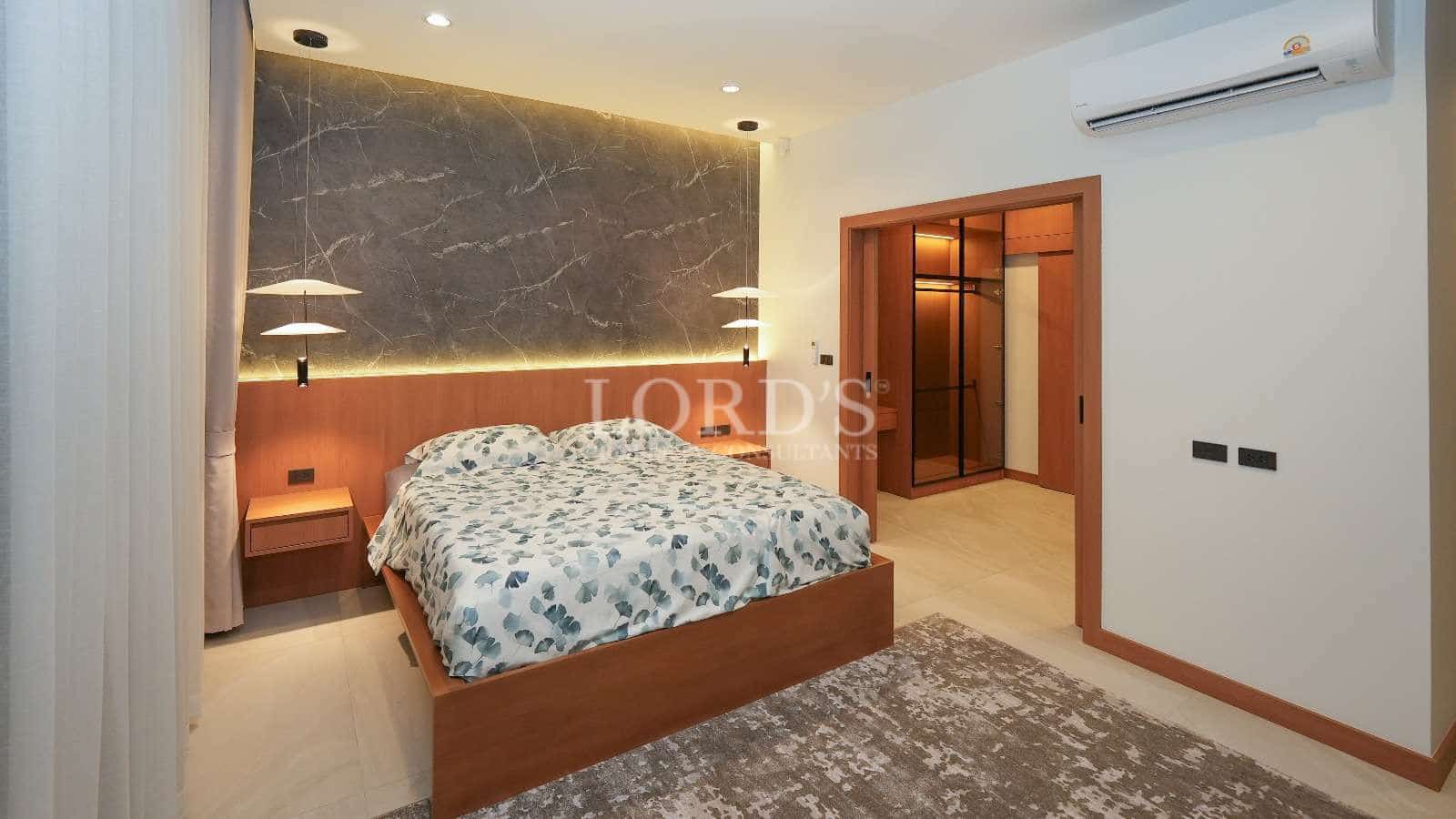 Modern luxury bedroom with wooden bed frame, marble accent wall, pendant lighting, and walk-in wardrobe.