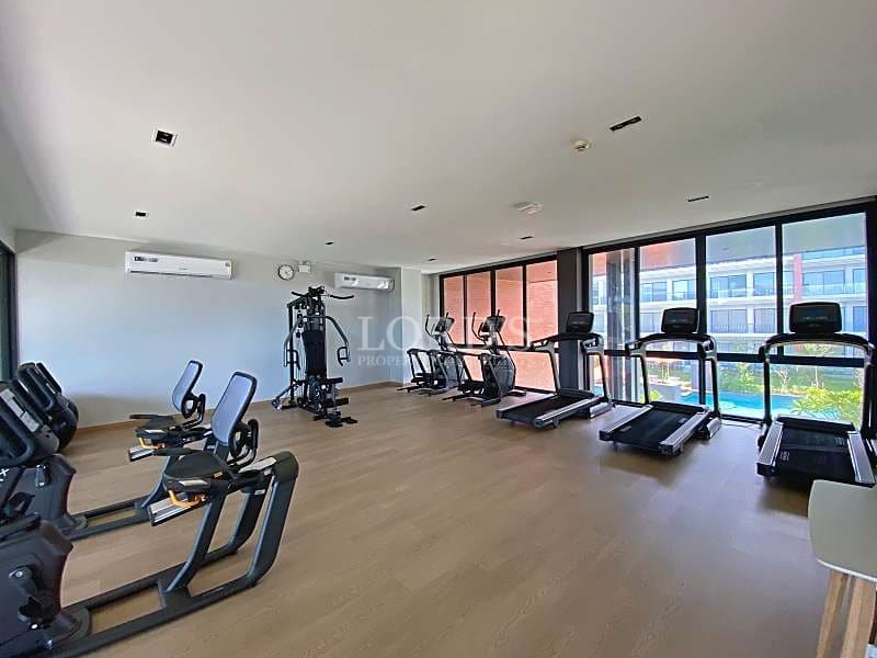 Modern apartment gym with treadmills, exercise bikes, strength equipment, and large floor-to-ceiling windows.