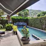 Private swimming pool with shaded patio, tropical plants, privacy hedges, and hillside views.