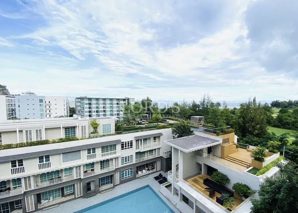 Elevated view of a modern residential complex with balconies, rooftop terraces, swimming pool, and surrounding greenery.