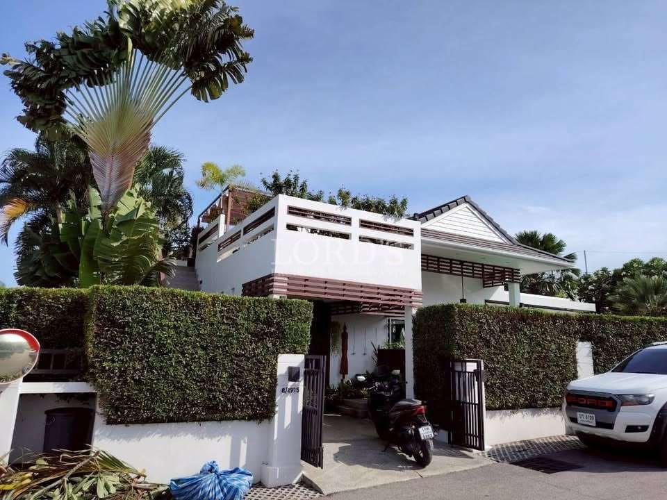 Modern two-story house with rooftop terrace, white exterior walls, privacy hedges, and gated entrance.