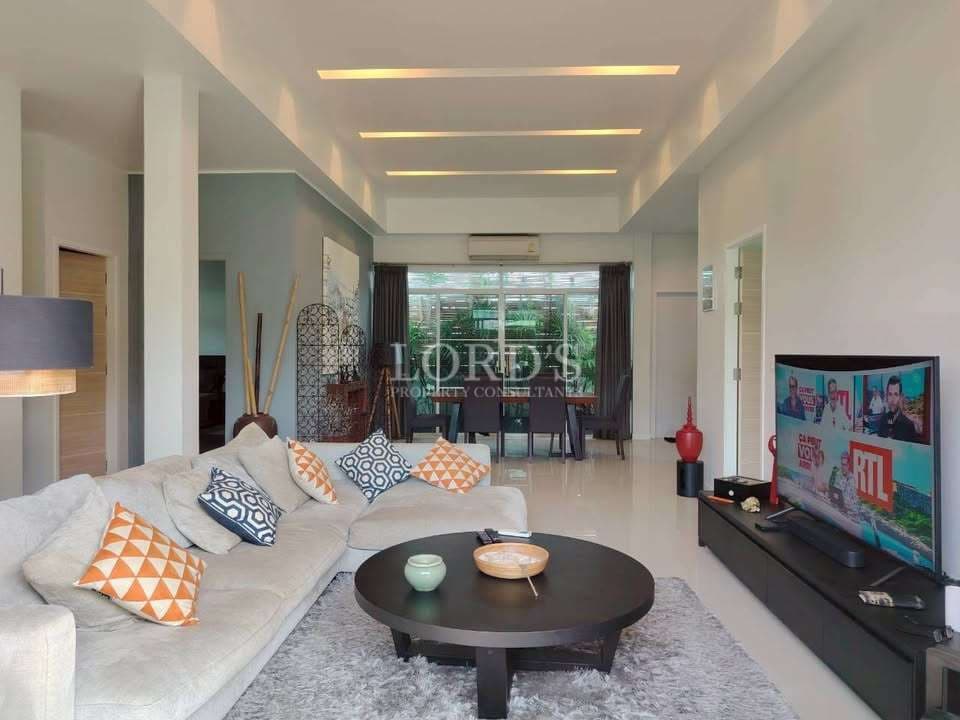 Modern open-plan living room with sectional sofa, coffee table, TV console, recessed ceiling lighting, and dining area.