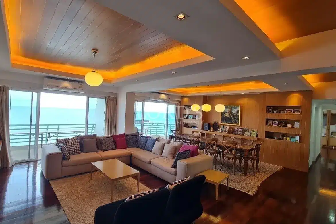 Spacious open-plan living and dining area with warm ceiling lighting, modern furniture, and sea-view balcony.