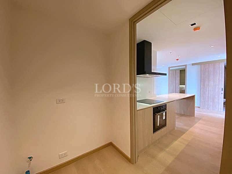 Modern apartment utility room next to an open kitchen with built-in oven, island counter, and wood flooring.