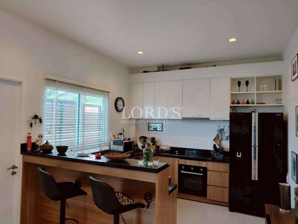 Modern open kitchen with island counter, bar stools, white cabinetry, built-in oven, and refrigerator.