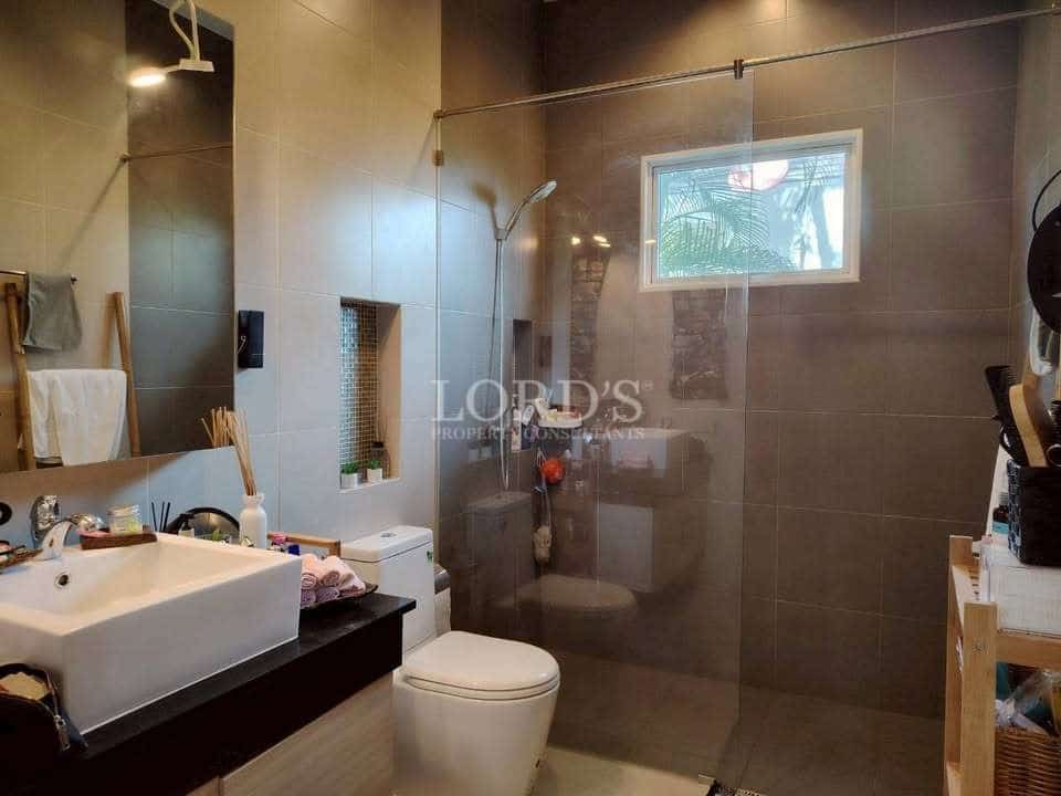 Modern bathroom with walk-in glass shower, wall-mounted vanity sink, neutral tiles, and compact window.