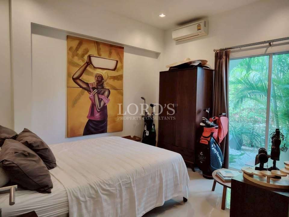 Cozy bedroom with white bedding, wooden wardrobe, air conditioning, sliding glass doors, and large artistic wall painting.