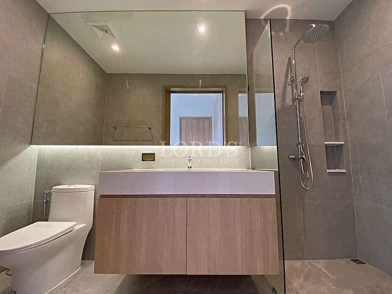 Modern bathroom with walk-in glass shower, rain showerhead, floating vanity, and neutral tile finishes.