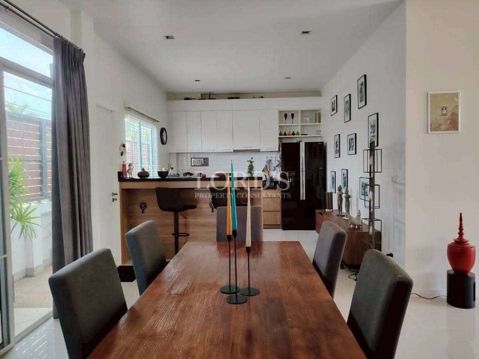 Modern open-plan dining and kitchen area with wooden dining table, bar seating, white cabinetry, and wall art.