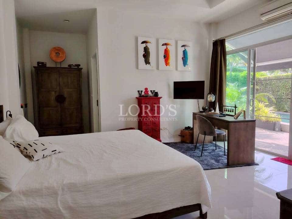 Bright bedroom with white bedding, wooden furniture, workspace desk, wall art, and sliding glass doors to a garden view.