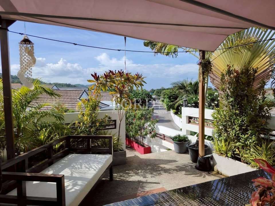 Cozy outdoor terrace with seating, shade canopy, tropical plants, and a peaceful residential street view.