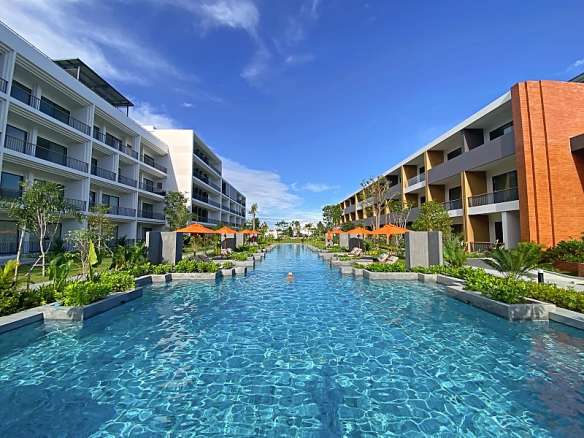 Luxury residential swimming pool between modern apartment buildings with landscaped gardens and clear blue water.