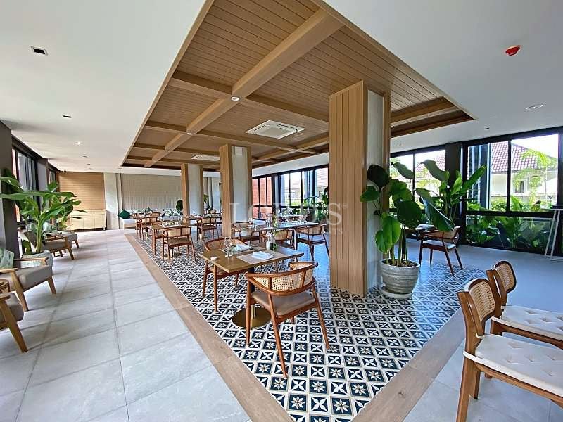 Modern open-air restaurant with wooden ceiling, stylish dining tables, indoor plants, and patterned tile flooring.