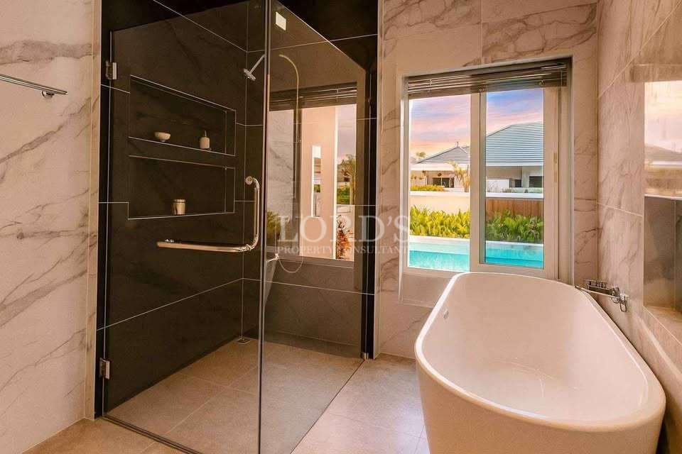 Luxury bathroom with freestanding bathtub, glass shower enclosure, marble walls, and pool view.